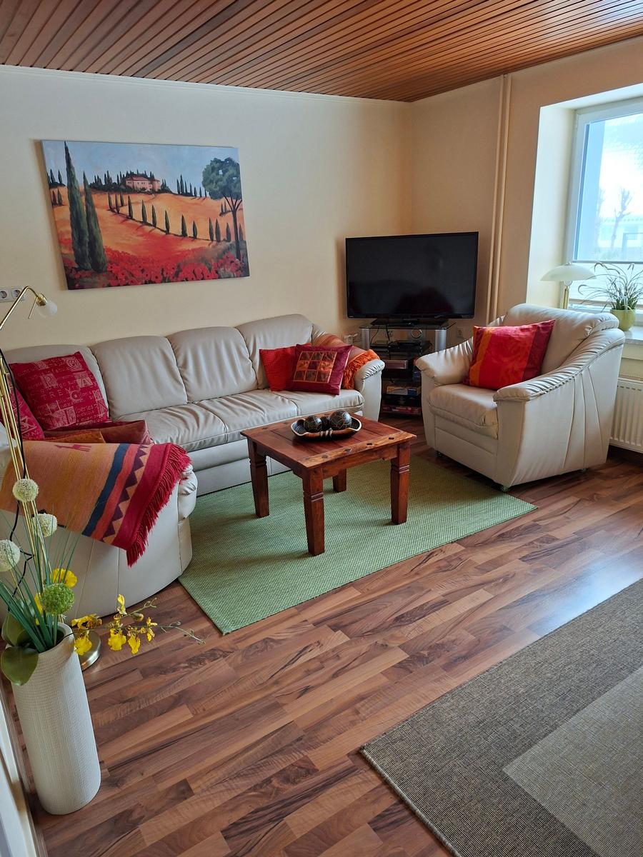 Wohnzimmer mit Sofa, Sessel, Fernseher und Holzboden.