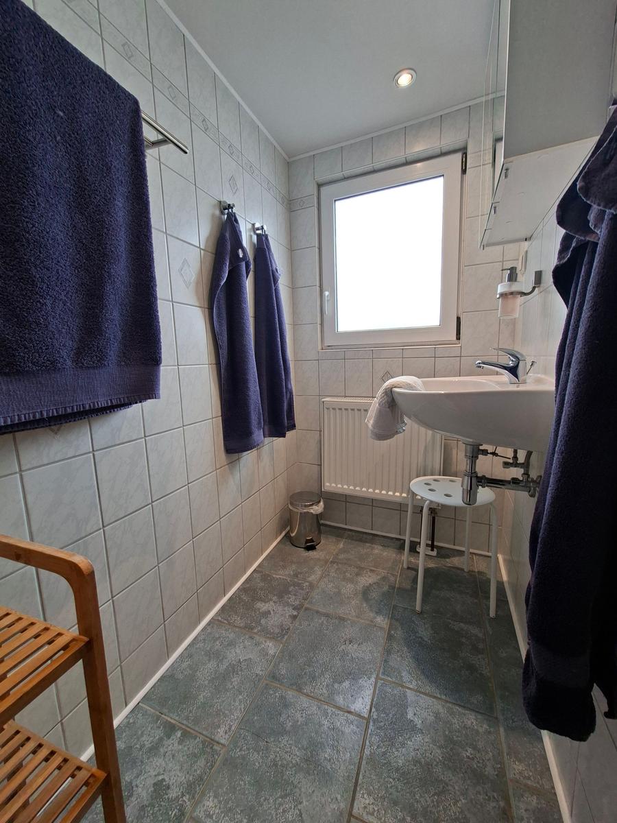 Badezimmer mit Waschbecken, Fenster, Handtuchhaltern und Bodenfliesen.