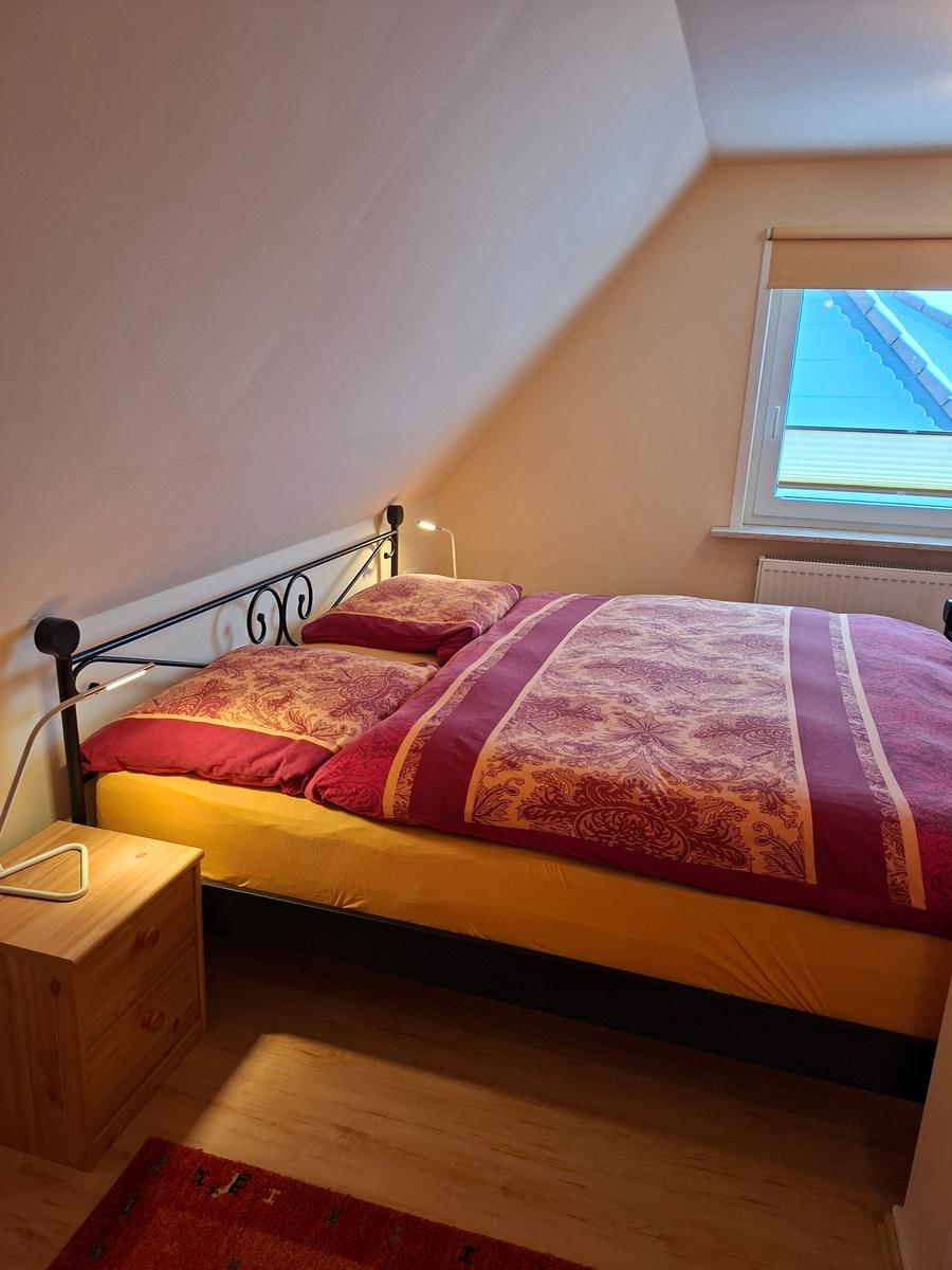 Schlafzimmer mit Dachschrägen, Bett mit gemusterter Bettwäsche und Holz-Nachttisch.