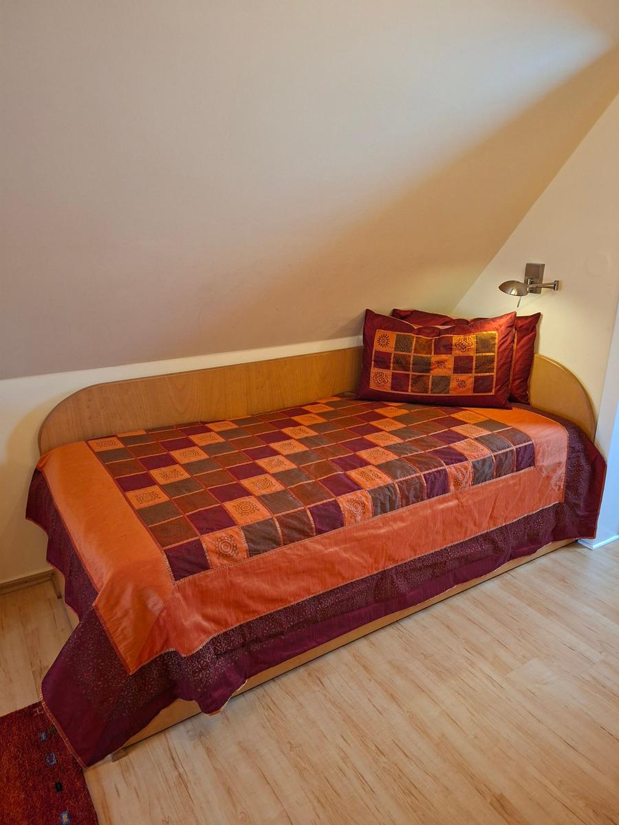 Schlafzimmer mit Dachschräge, Bett mit buntem Quilt und Holzboden.