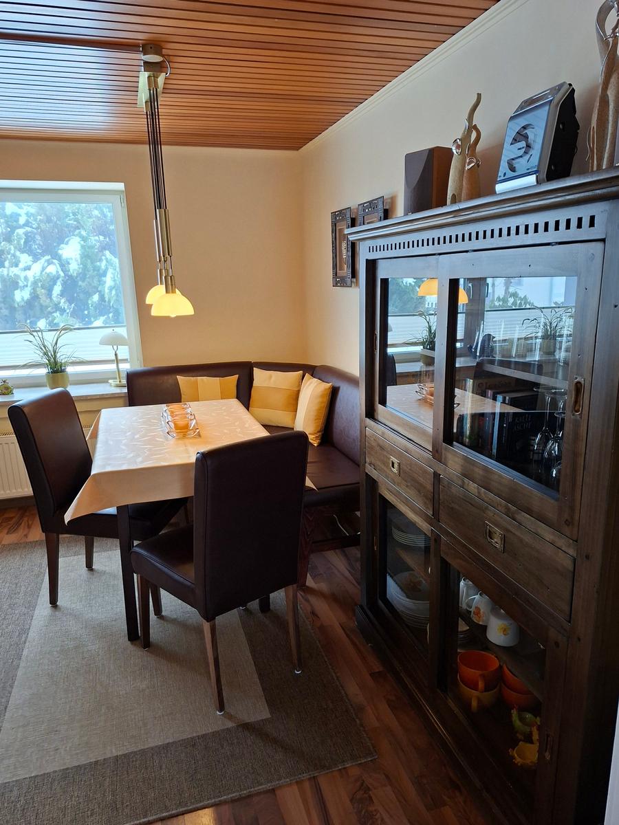 Esszimmer mit Tisch, Stühlen und Glasvitrine. Fenster mit Blick auf Außenbereich.