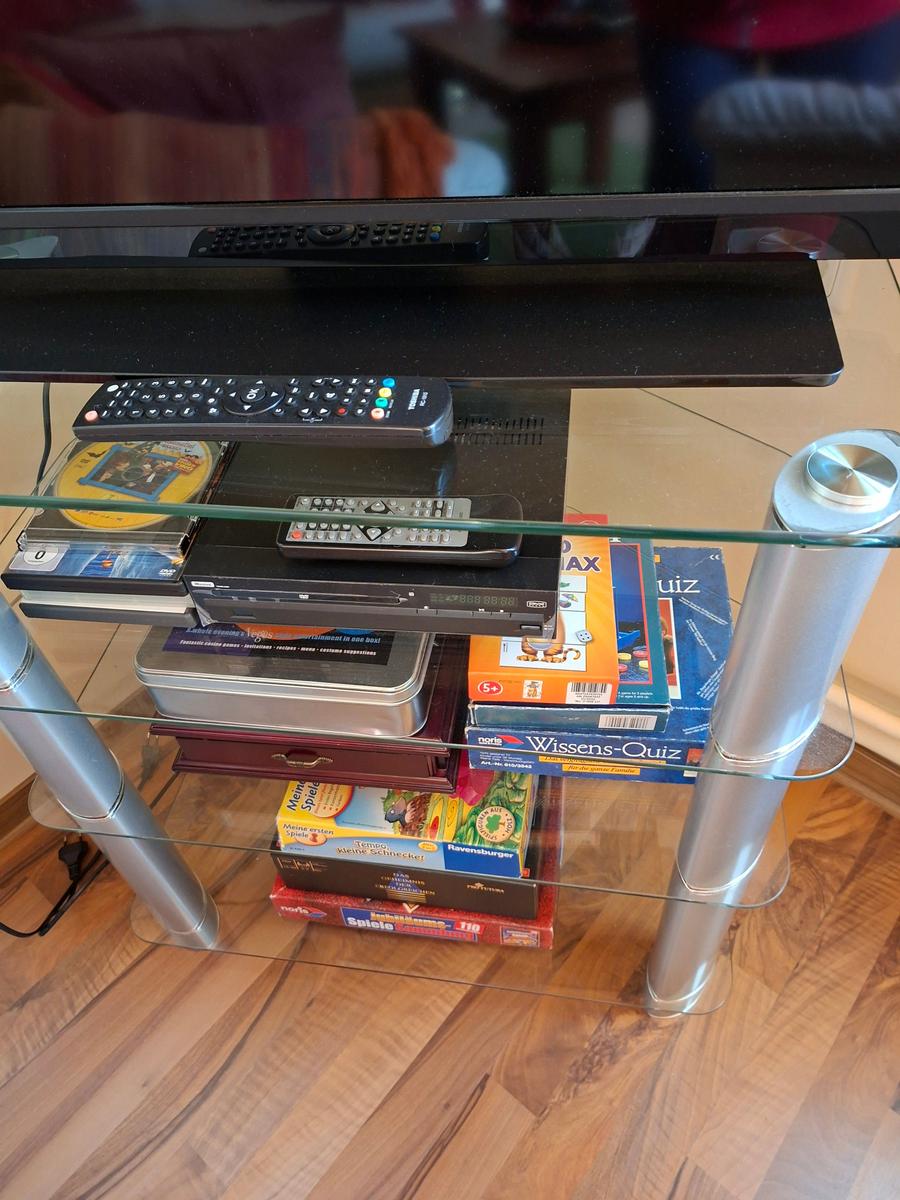 Glas-Tisch mit Fernseher, Fernbedienungen und Spielboxen auf mehreren Ebenen.