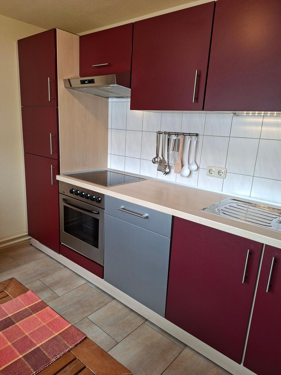 Küche mit roten Schränken, Edelstahlherd und weißen Fliesen.
