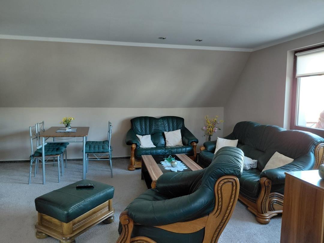 Wohnzimmer mit dunkelgrünem Ledersofa, Esstisch und Fenster