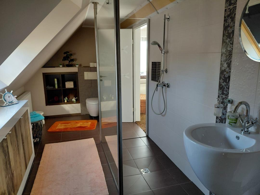 Badezimmer mit Dusche, Waschbecken und Toilette unter Dachschrägen.