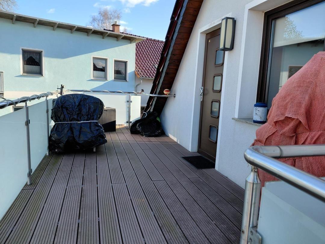 Terrasse mit Holzdeckung, Geländer und geschlossenen Möbeln.