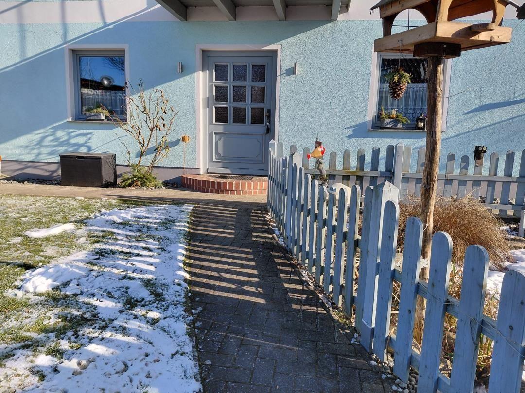Haus mit blauer Fassade, Eingangstür und gepflastertem Weg mit Schnee.