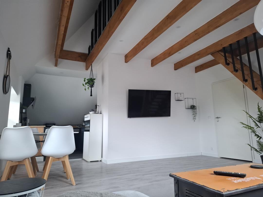 Wohnzimmer mit Holzbalken, Fernseher und Essbereich.