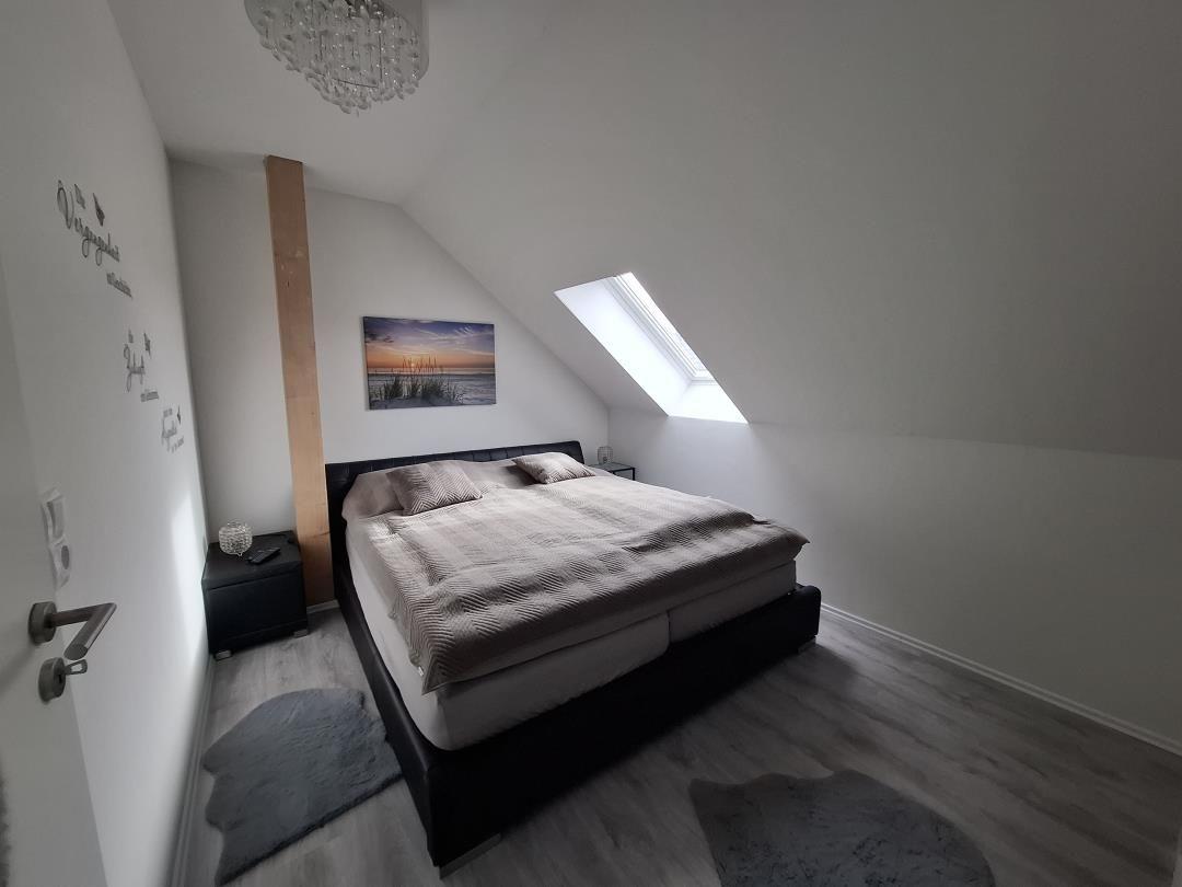 Schlafzimmer mit Dachschrägen, Bett, Fenster und Wandbild.