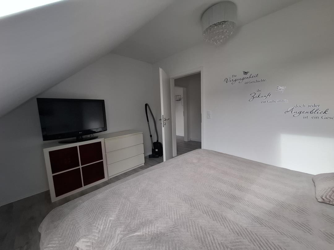 Schlafzimmer mit Dachschrägen, Bett, Fernseher und Wanddekoration.