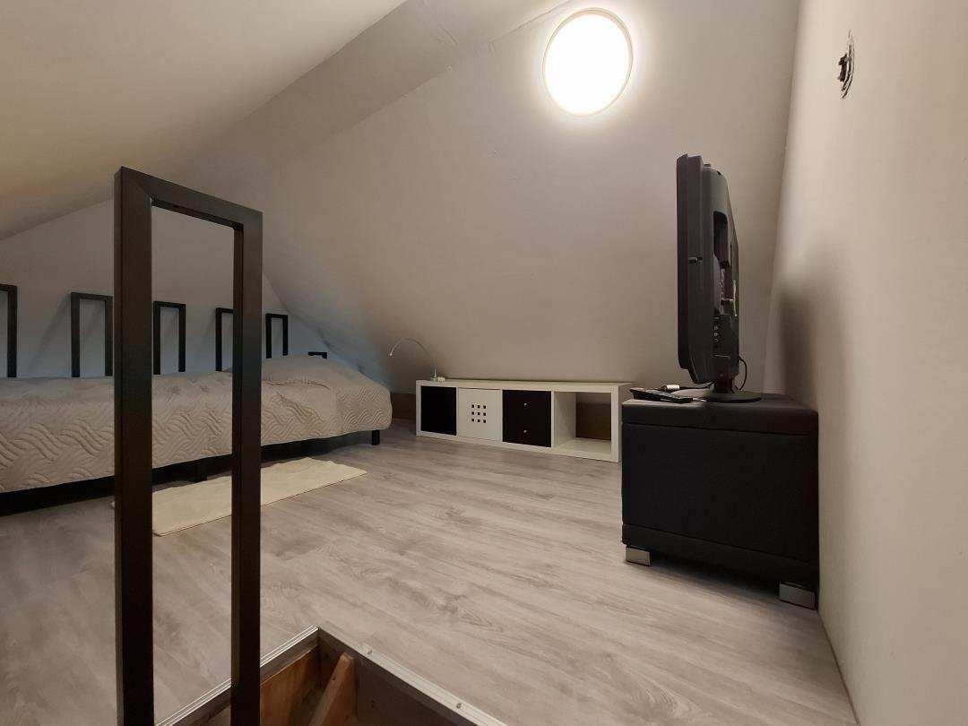 Schlafzimmer mit Dachschrägen, Bett, TV und Holzboden.