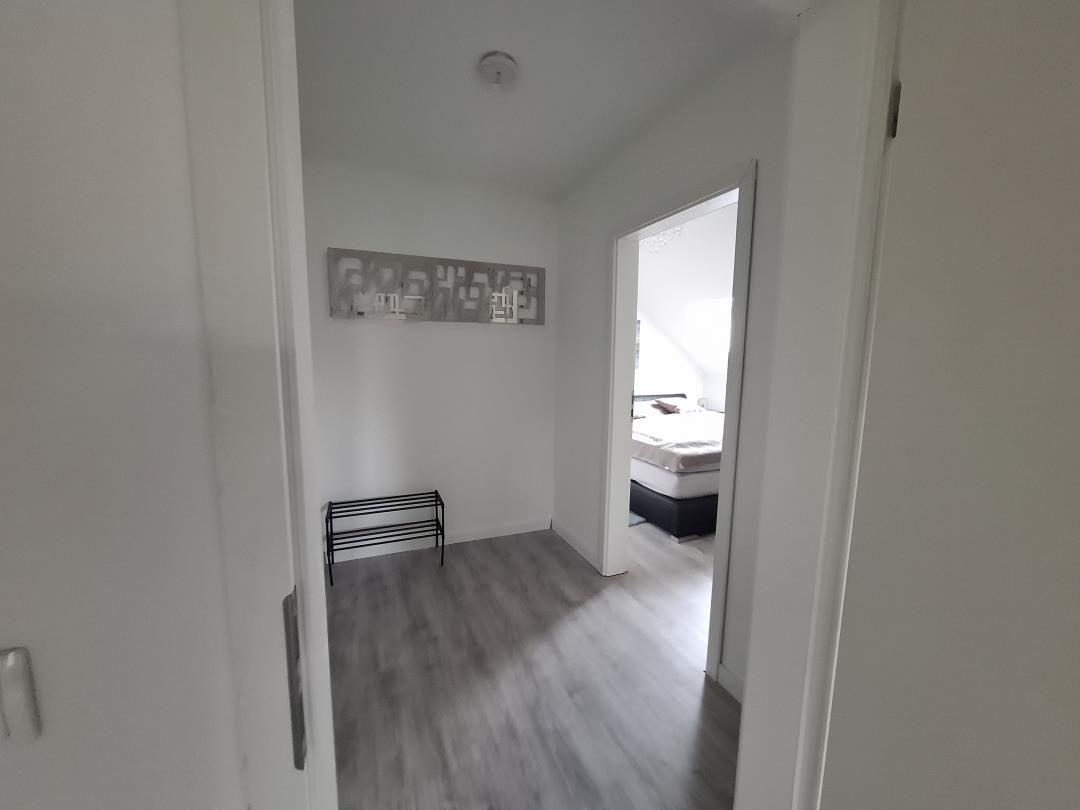 Flur mit grauem Boden und Blick in Schlafzimmer mit Bett.