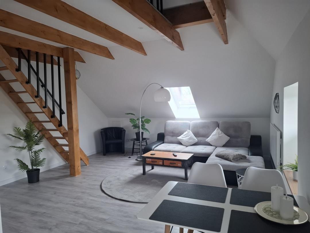 Wohnraum mit Dachschrägen, Sofa, Tisch und Stühlen. Treppenaufgang zur oberen Etage.