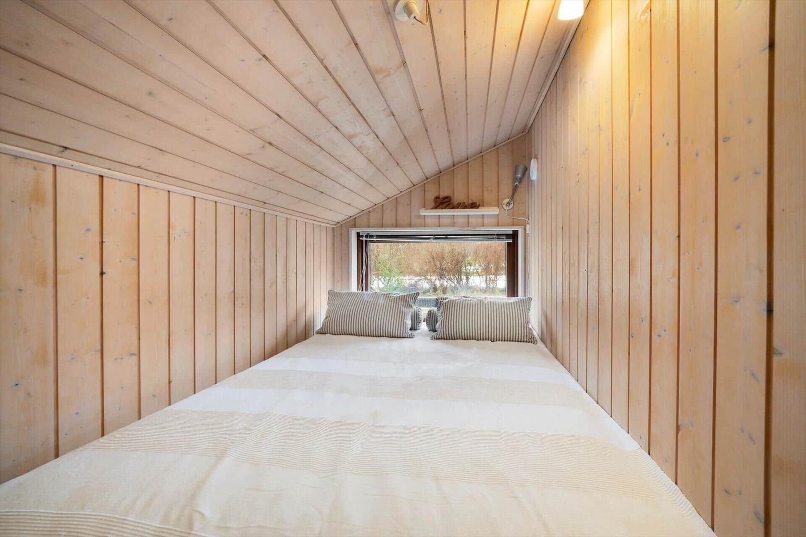 Bedroom with wooden walls and bed under sloped ceiling
