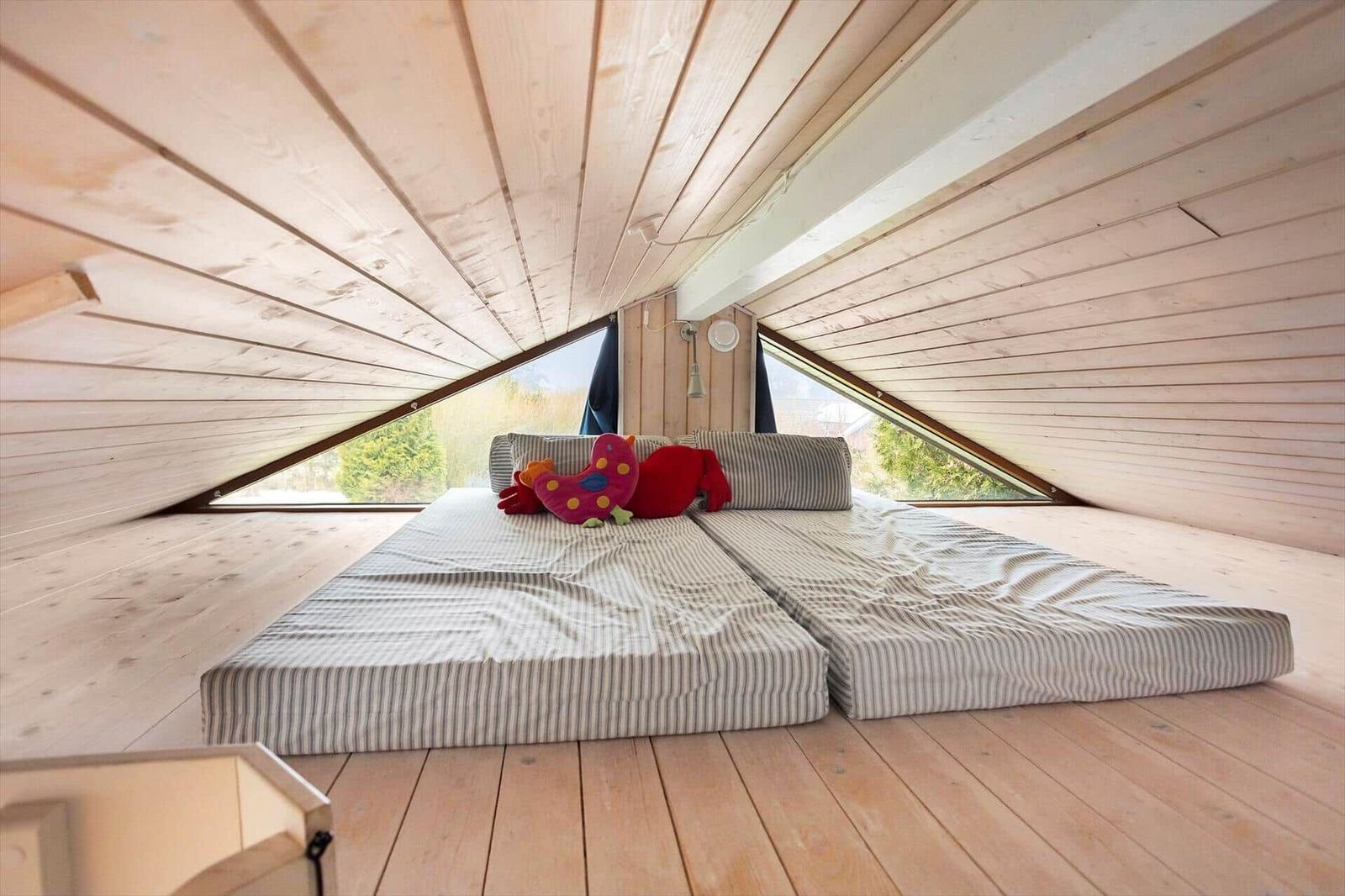 Bedroom with double bed under wooden roof, large window, toys on bed.
