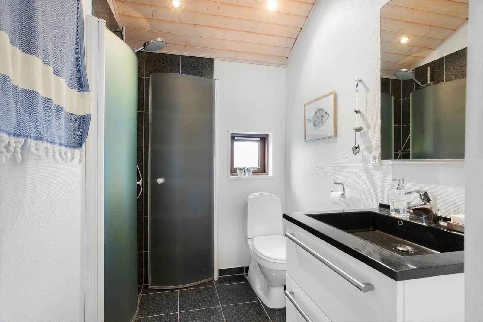 Bathroom with shower, toilet, and sink. Wooden ceiling and window.