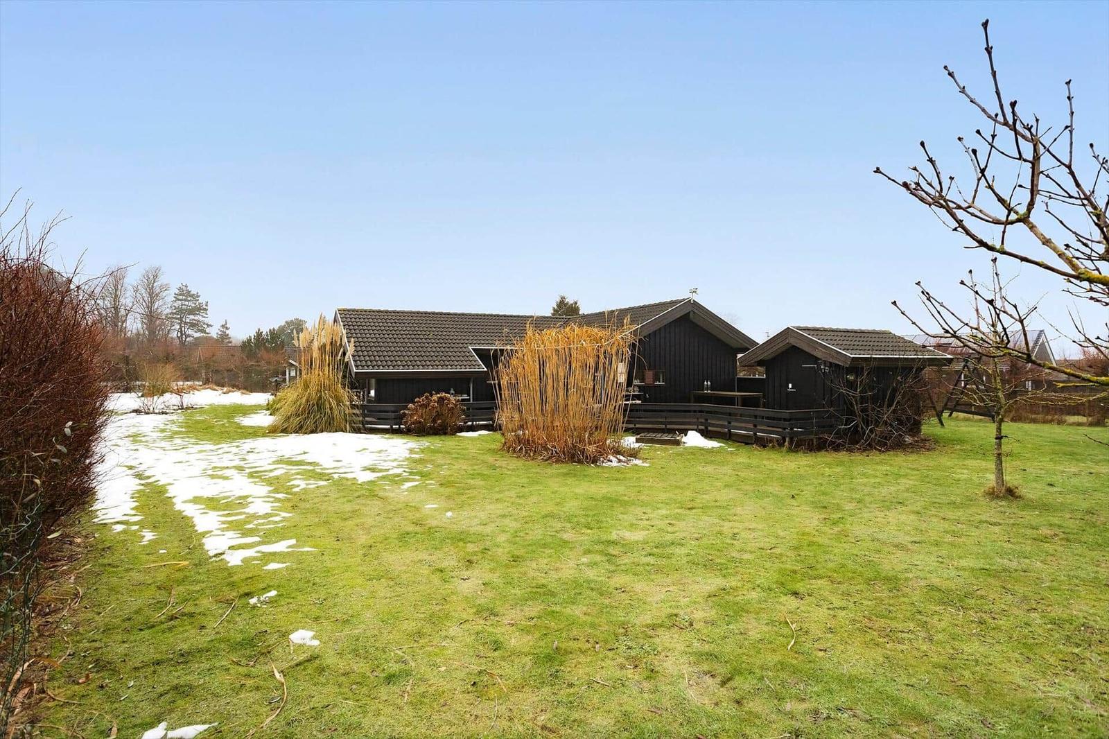 Black wooden cabins with terrace on a green lawn with patches of snow.