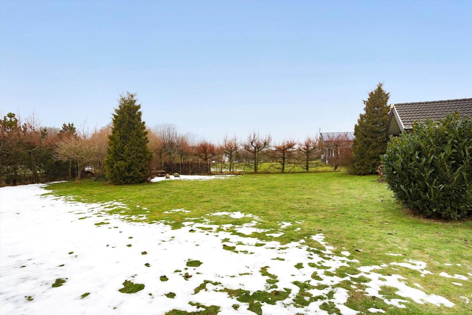 Lawn with grass and snow, trees, and part of a house.