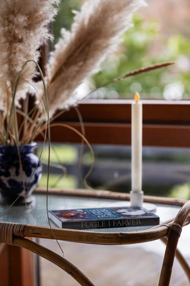 On a round table, there is a book, a candle, and a plant in a blue pot.