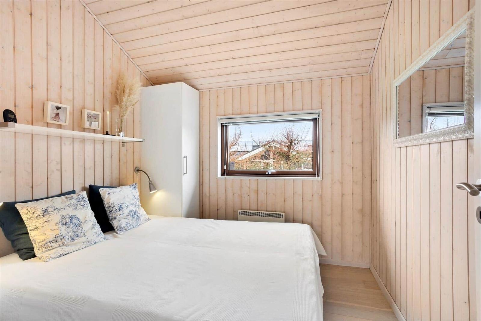 Bedroom with wooden walls, bed, window, and mirror.