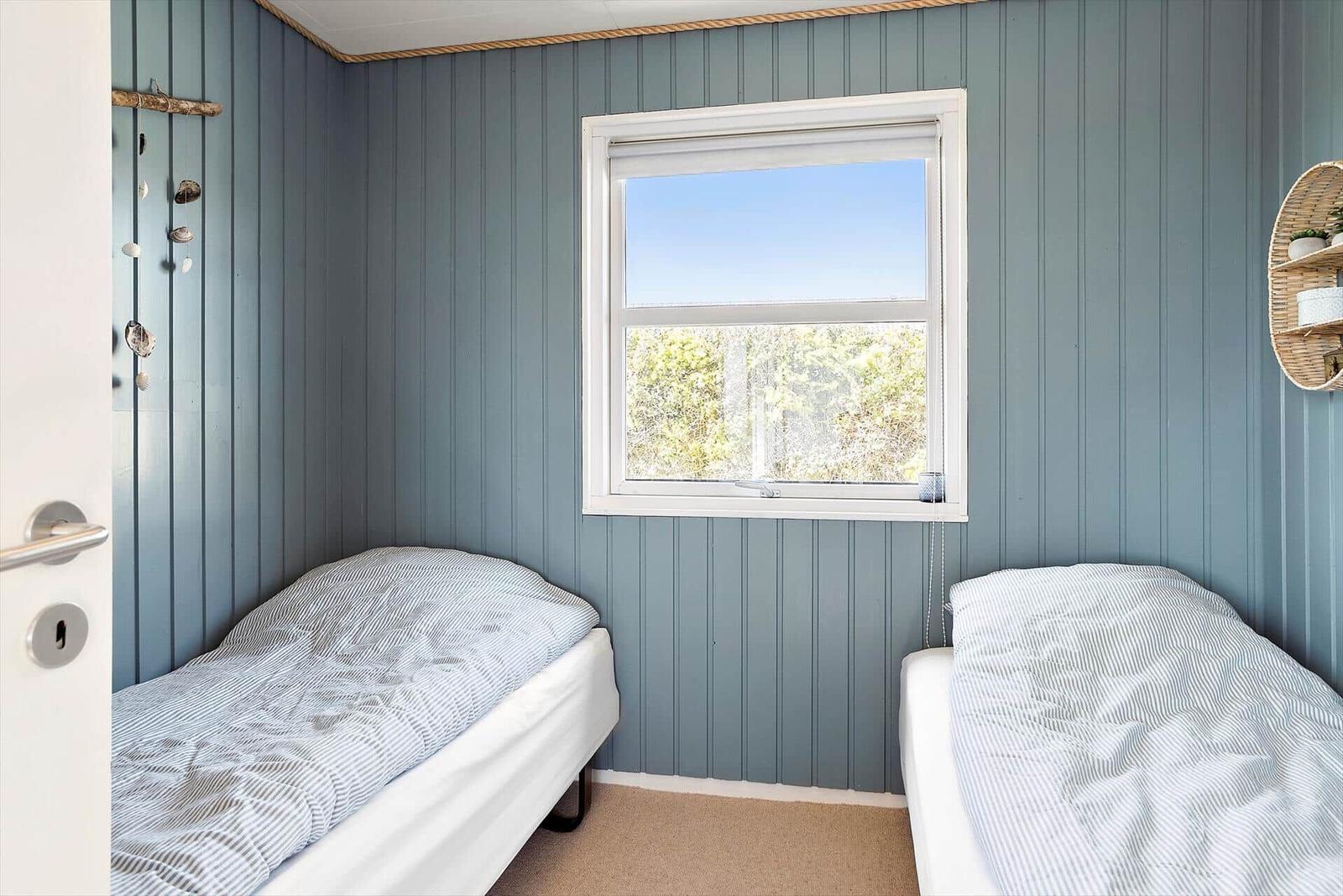 Two beds in a room with blue walls and a window.
