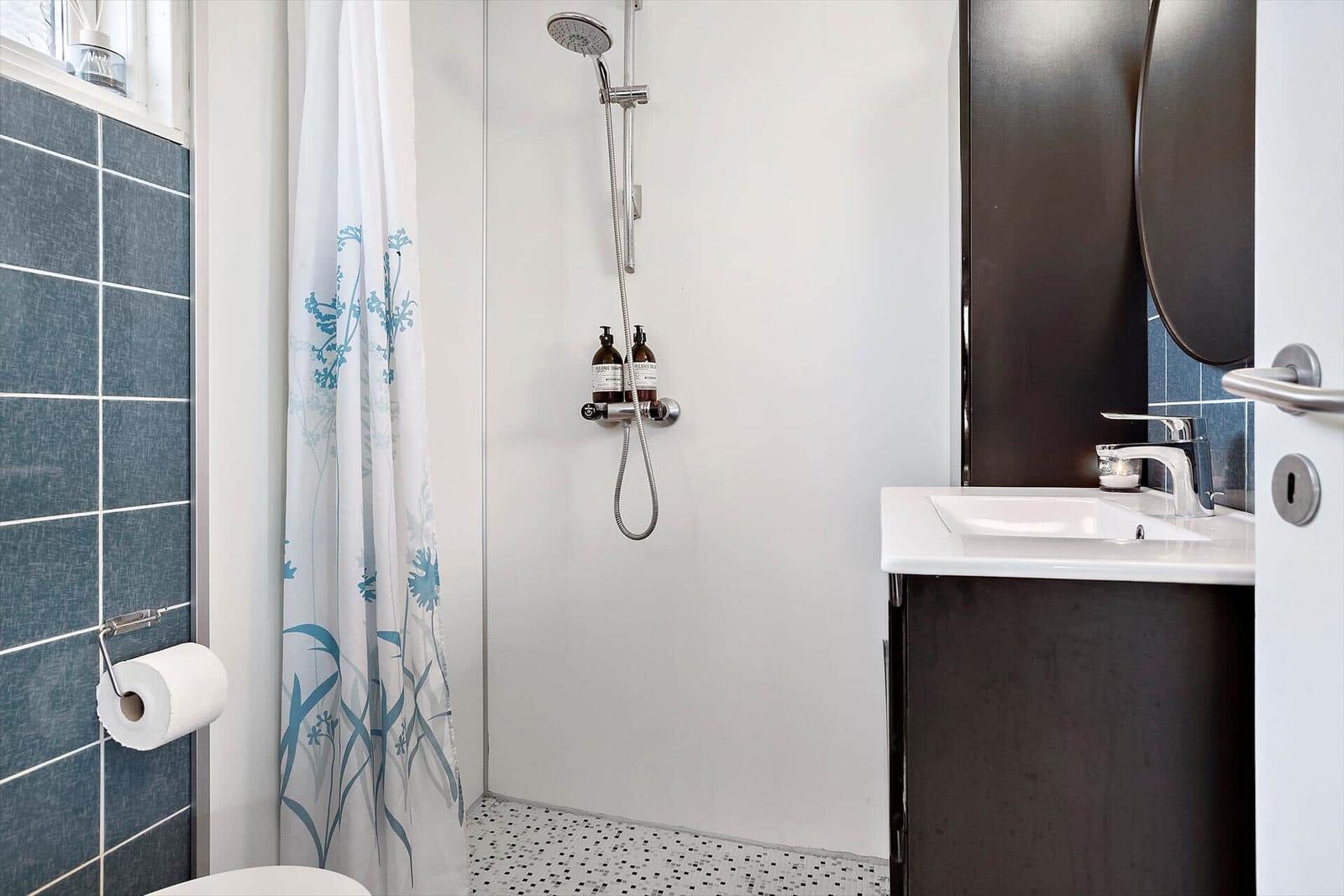 Bathroom with shower, sink, and toilet. Tiled wall and shower curtain with floral pattern.