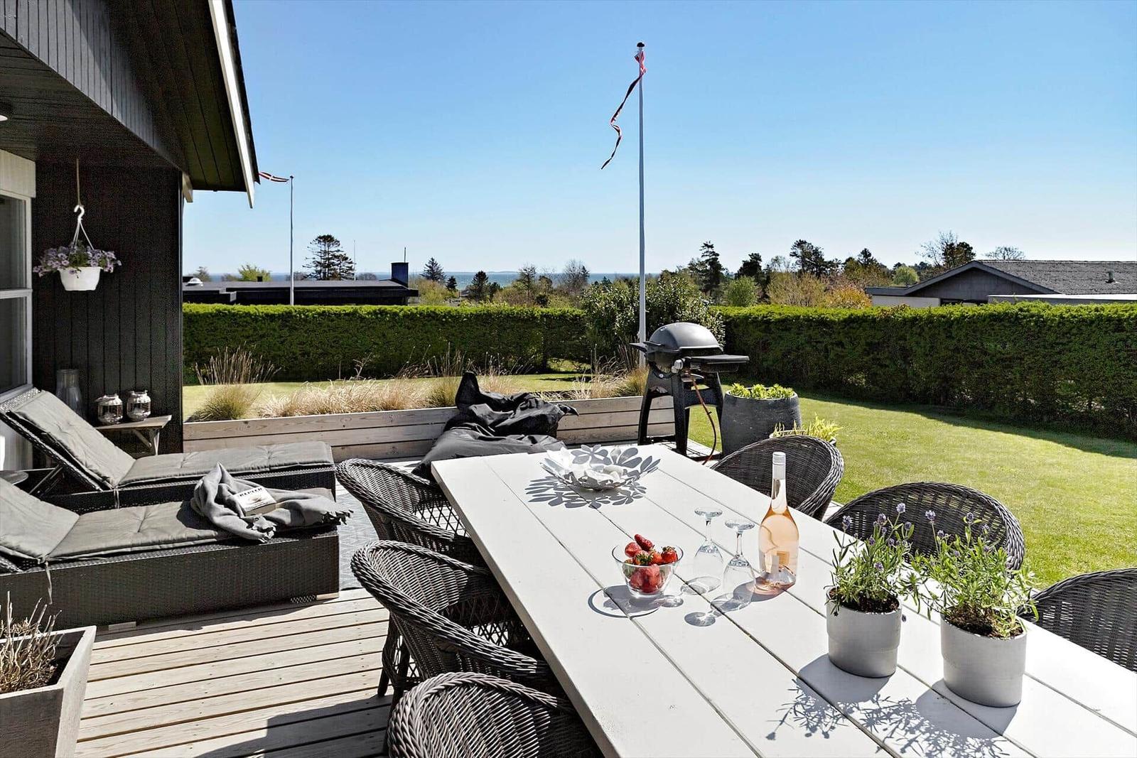 Terrace with table, chairs, grill, and view of green lawn.