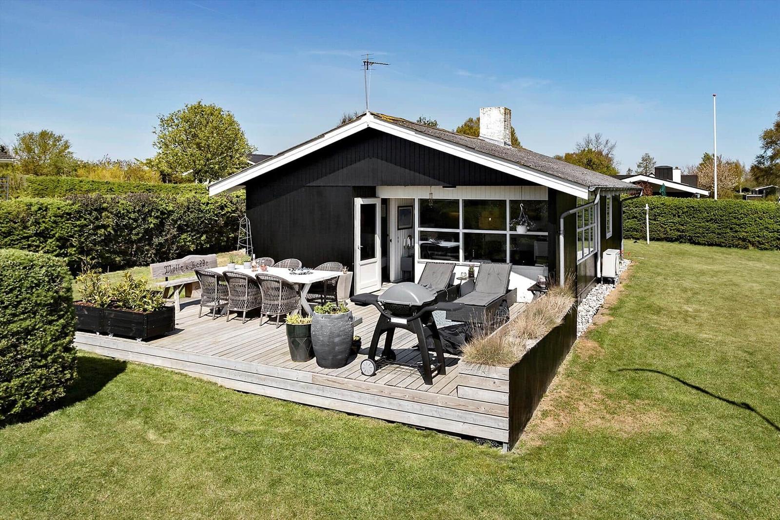 Black house with terrace, grill, and garden furniture. Surrounded by greenery.