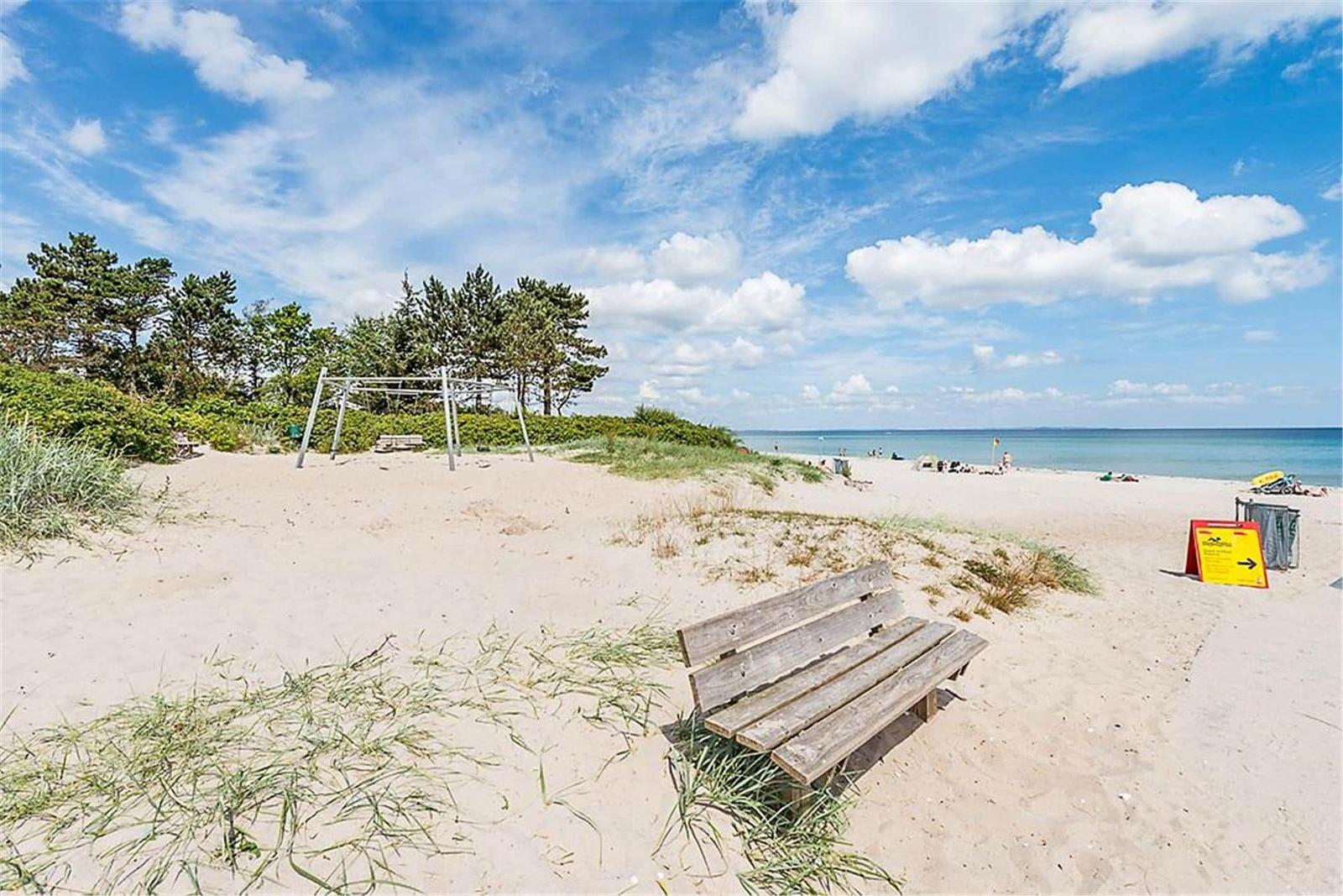 Wooden bench on sandy beach with view of sea and playground.