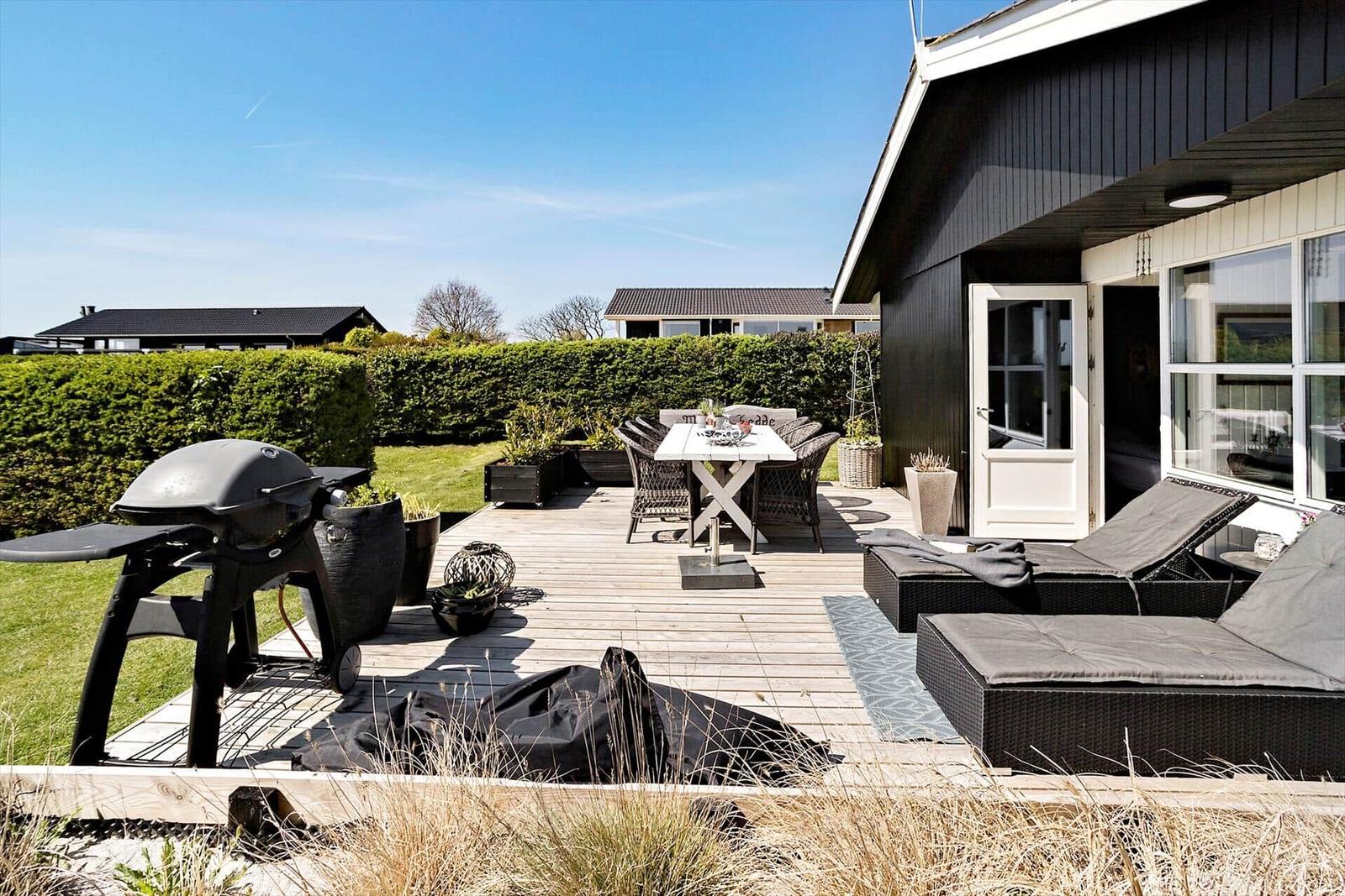 Deck with grill, table, chairs, and loungers in front of a house.