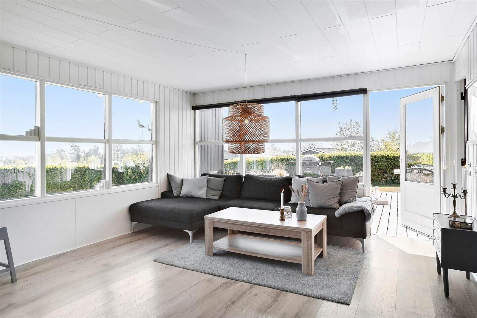 Living room with dark sofa, wooden coffee table, and large windows. Outside is a terrace.