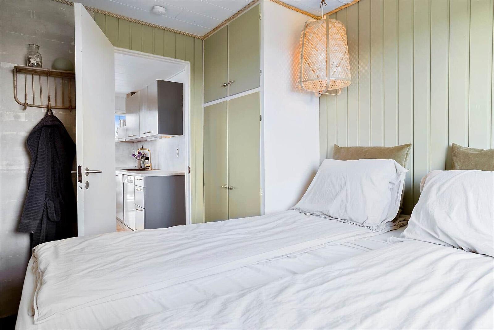 Bedroom with bed, coat rack, and view into the kitchen.