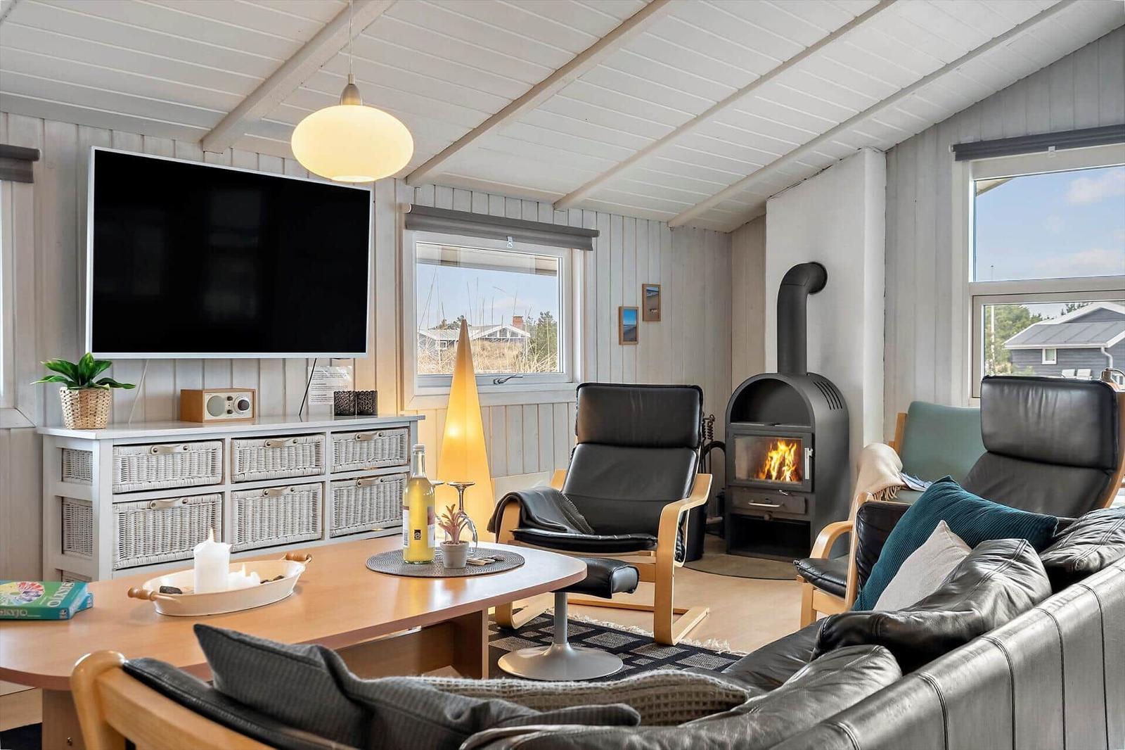 Wohnzimmer mit Kamin, Sofa, Sessel und Fernseher an Wand.