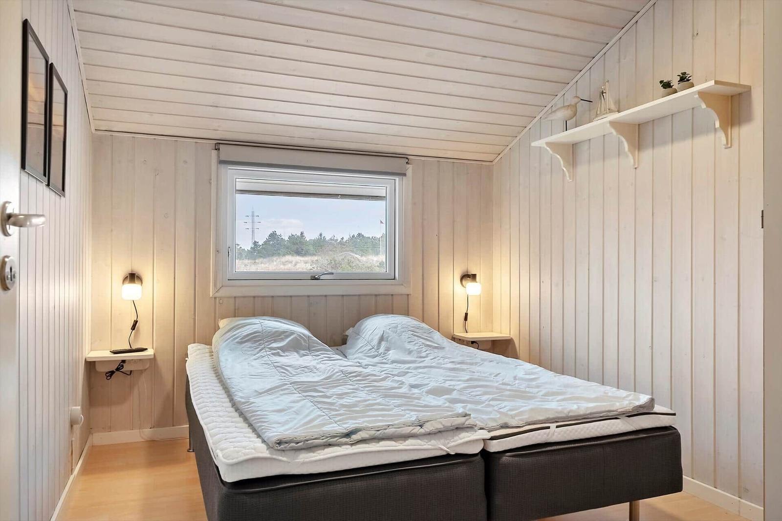 Schlafzimmer mit Bett, Fenster und Holzwandverkleidung.