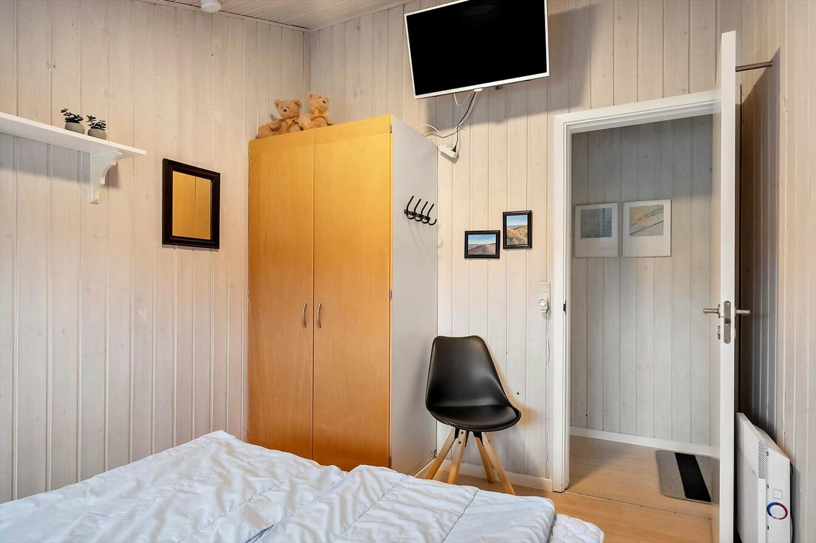 Schlafzimmer mit Bett, Kleiderschrank, TV und Stuhl.