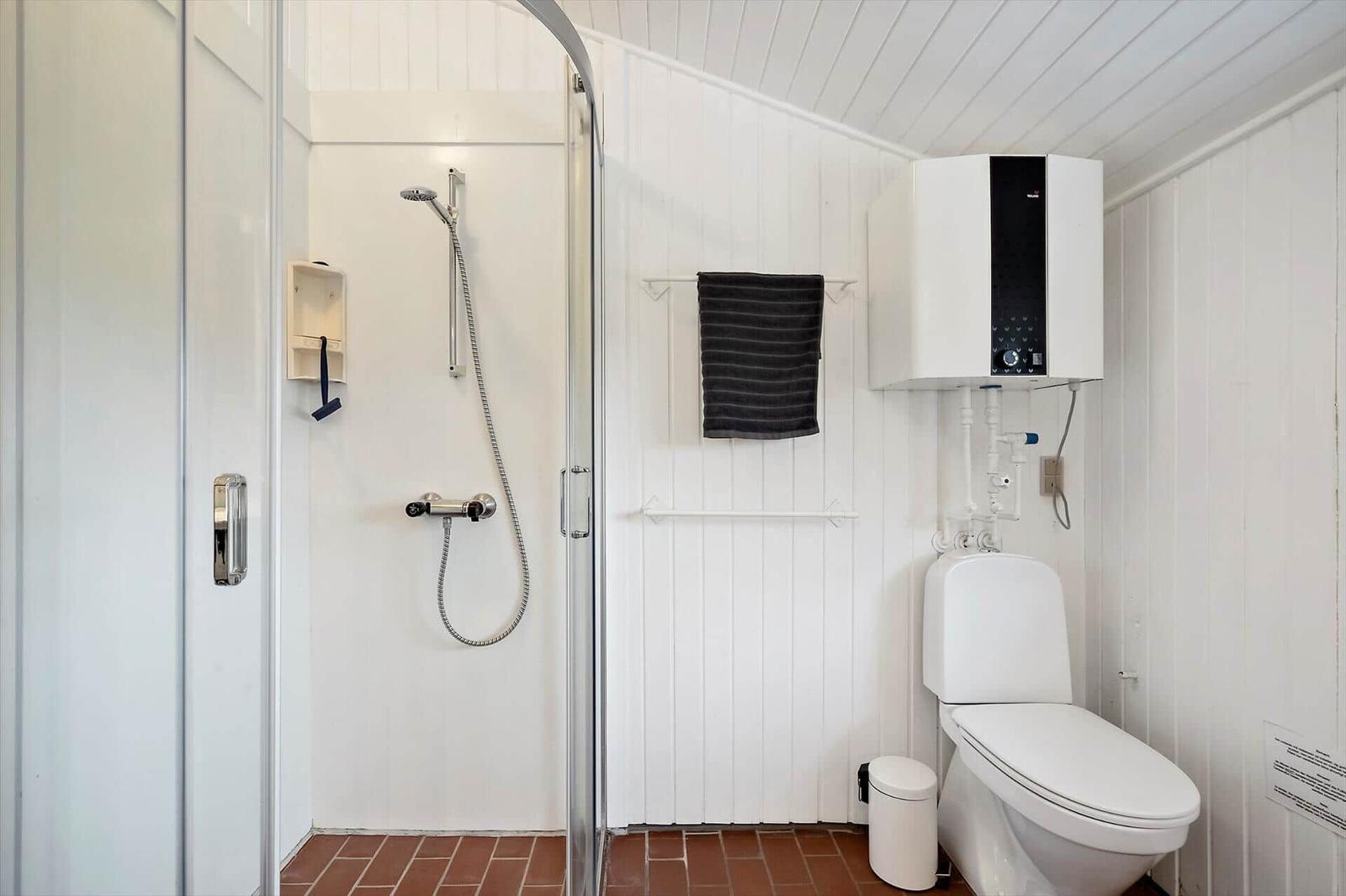 Badezimmer mit Dusche, Toilette und Heizung. Fliesenboden und weiße Wände.