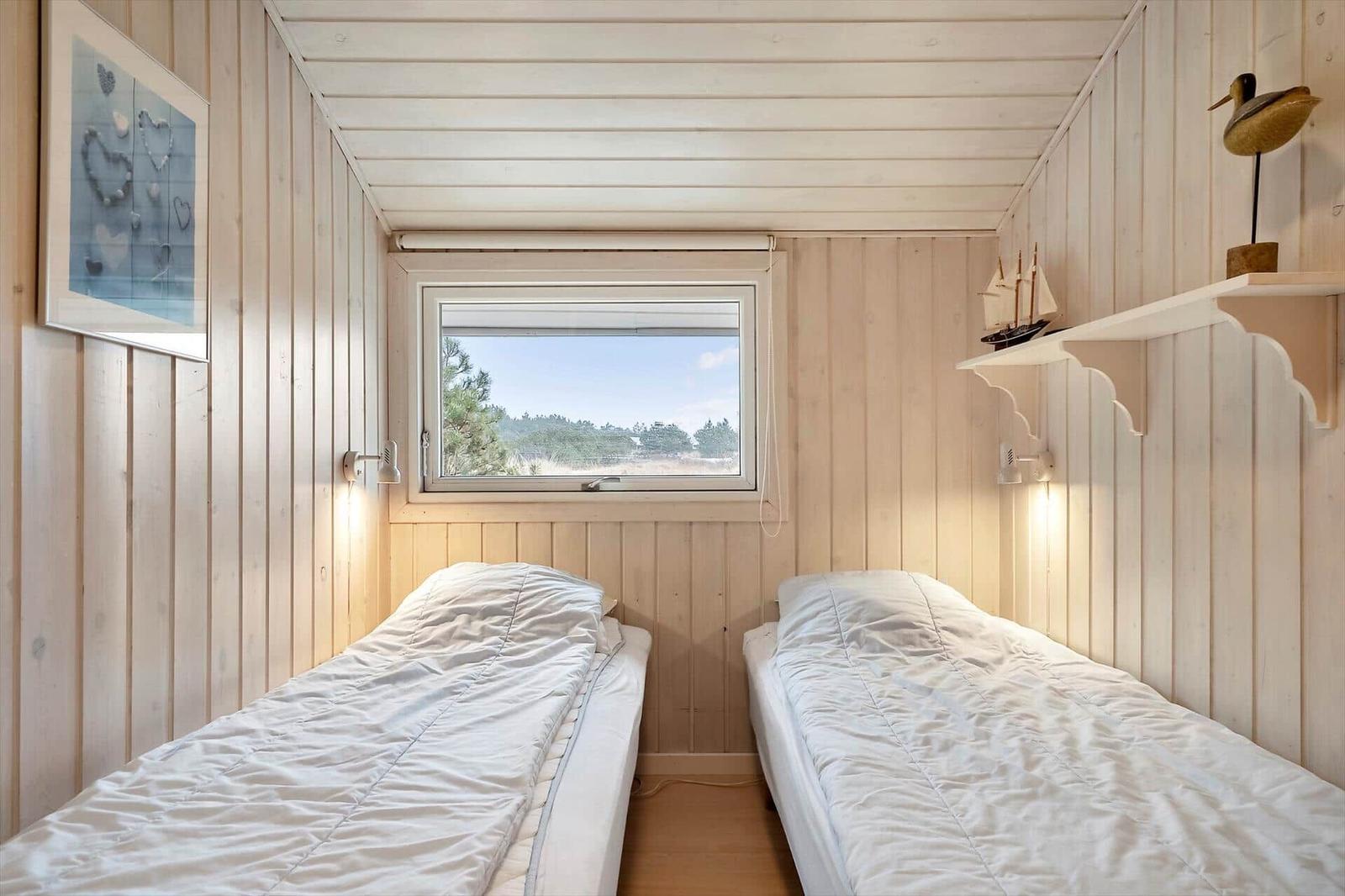 Zwei Betten in einem Holzraum mit Fensterblick auf Wald.