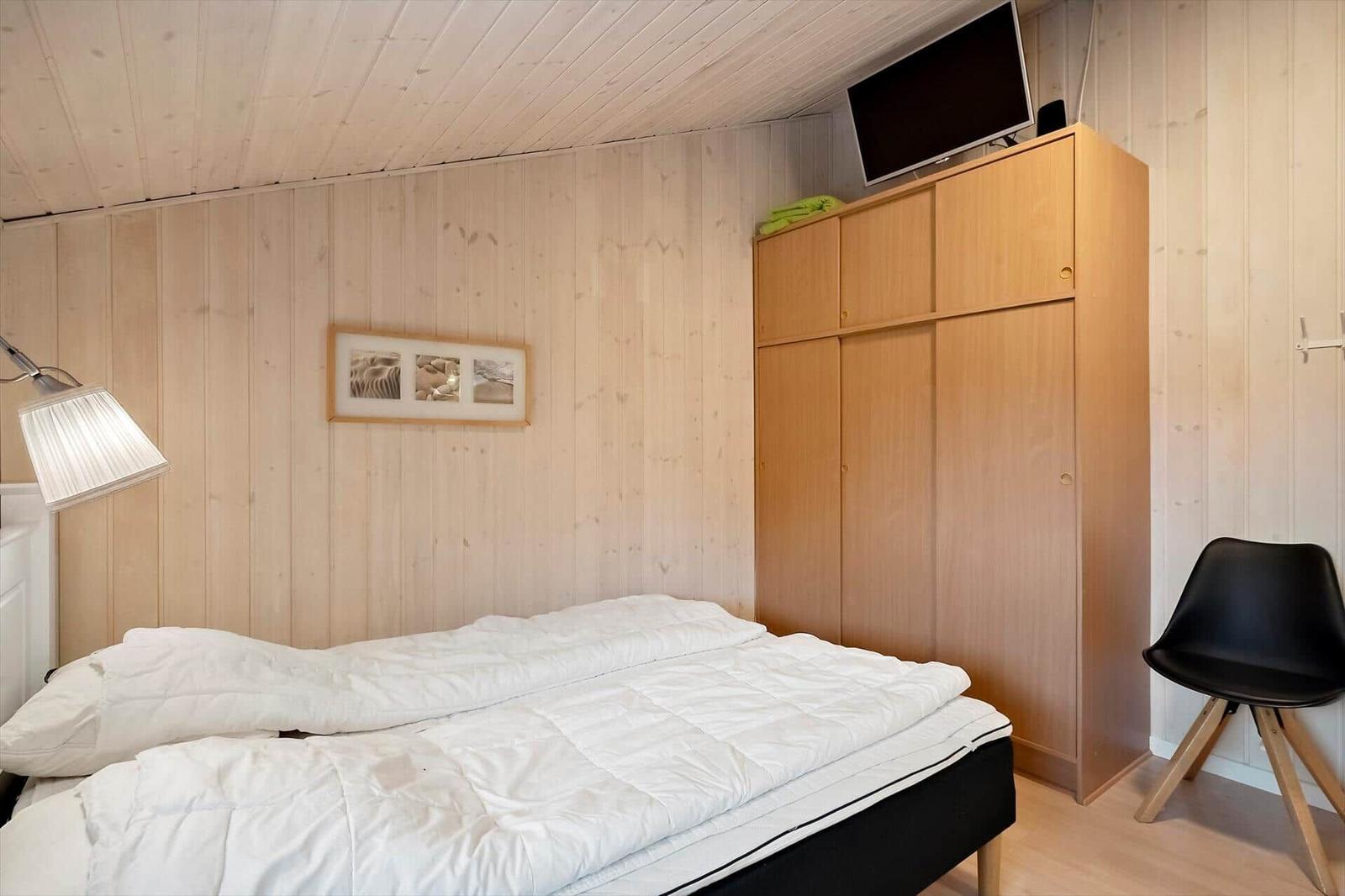 Schlafzimmer mit Bett, Kleiderschrank und Fernseher an der Wand.