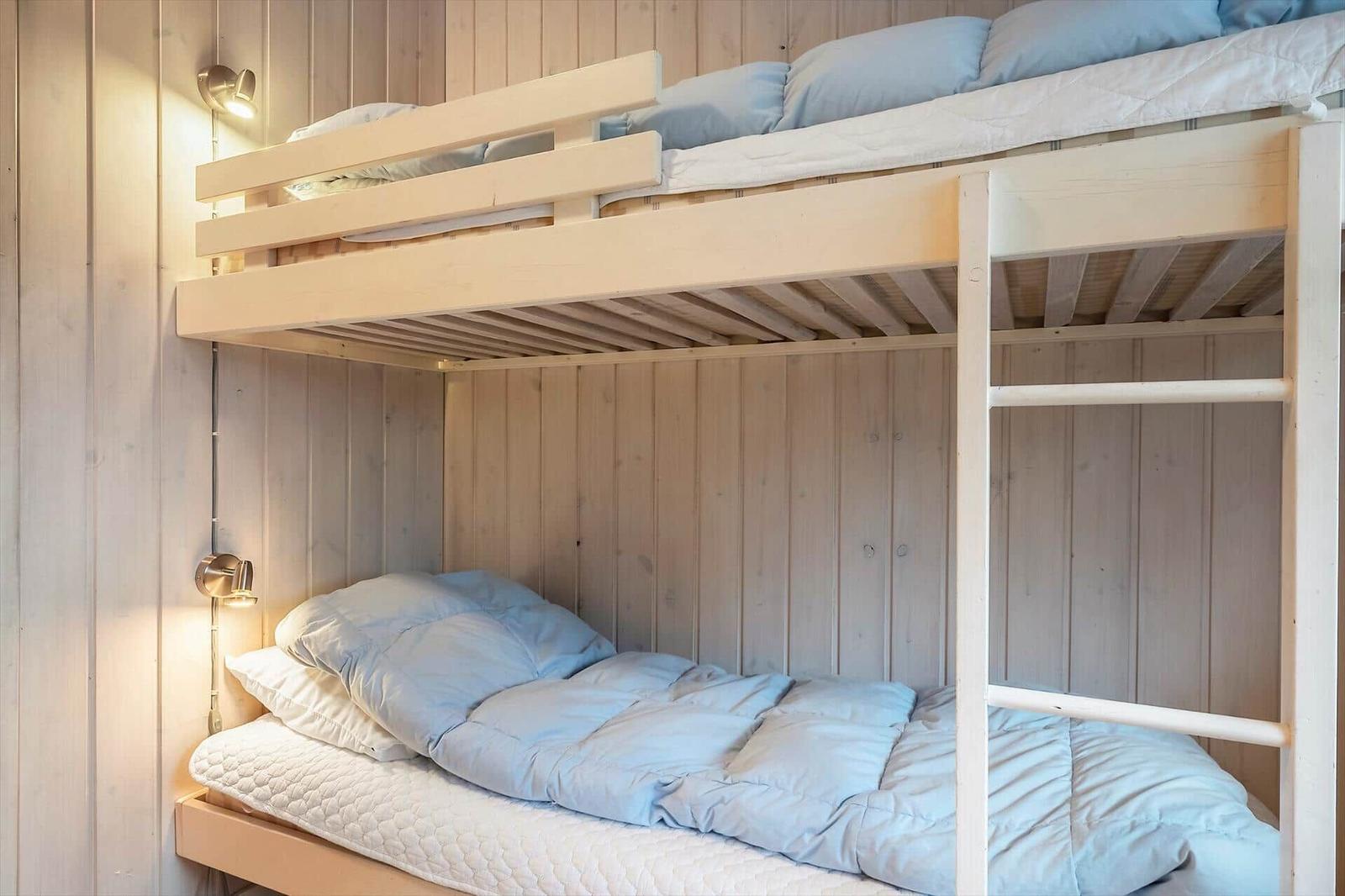 Doppelstockbett mit Matratzen und hellblauen Kissen in Holzwandnische.