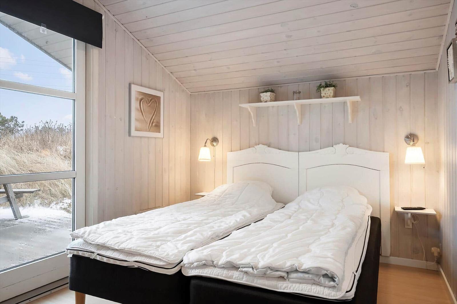 Schlafzimmer mit Doppelbett, Holzwand und Fensterblick auf Außengelände.