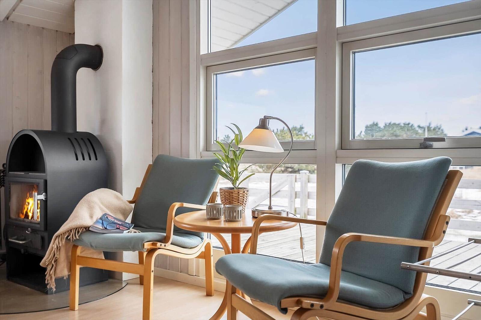 Zwei Sessel und ein Kamin stehen vor großen Fenstern mit Blick auf den Außenbereich.