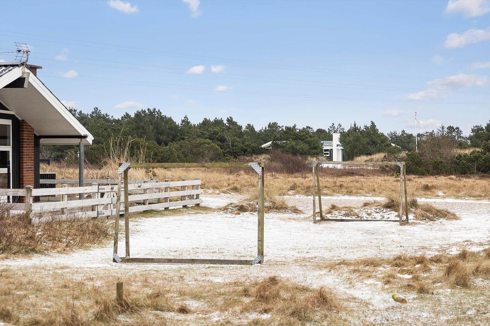 Haus mit Fußballtor und weißem Zaun auf sandigem Grund.