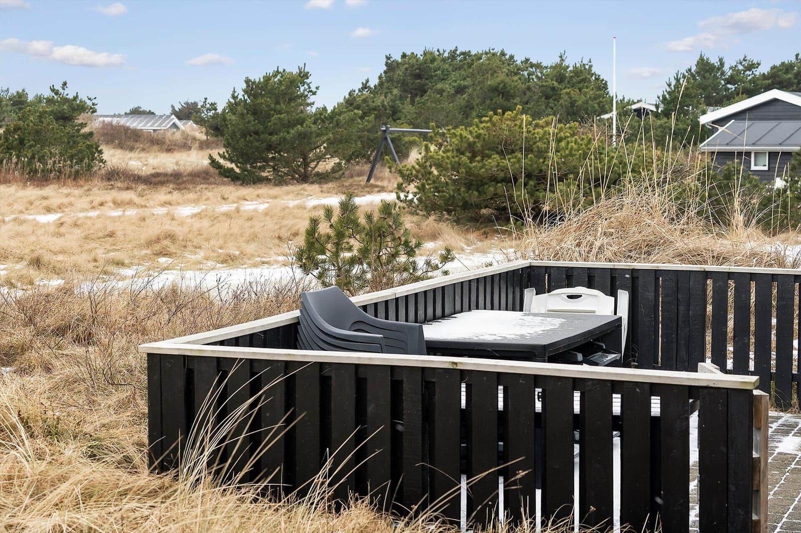 Terrasse mit Tisch und Stühlen, umgeben von Hecken und Gras.