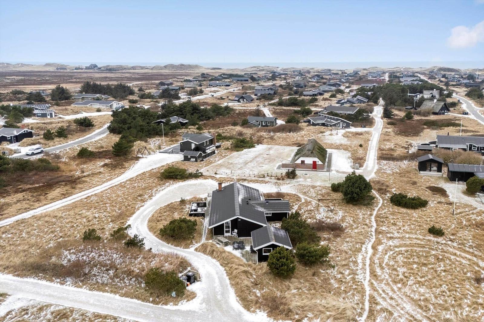 Haus mit Terrasse und Grillplatz in dünner Vegetation.