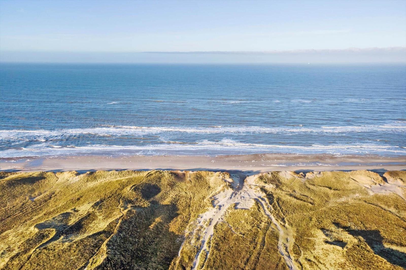 Ausblick auf Strand und Meer mit Dünen im Vordergrund.