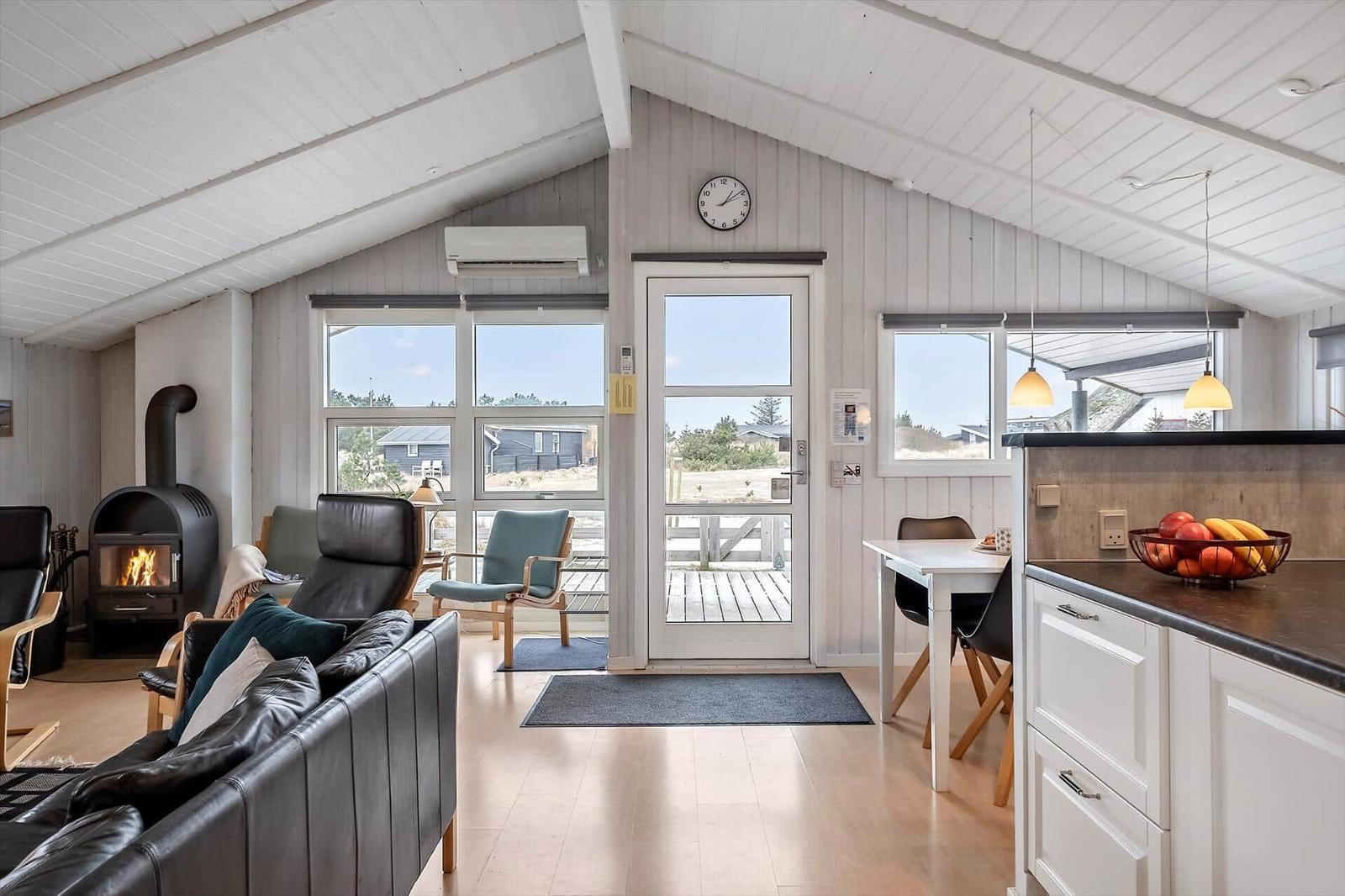 Wohnbereich mit Kamin, Essplatz und Küchenzeile. Durchgang zur Terrasse mit Blick auf den Außenbereich.