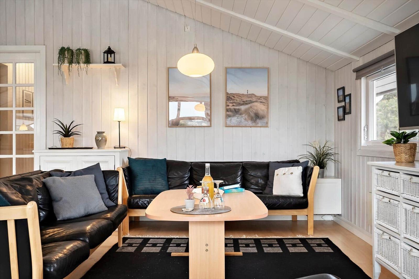 Wohnzimmer mit schwarzen Ledersofas, Holztisch und weißen Wänden.