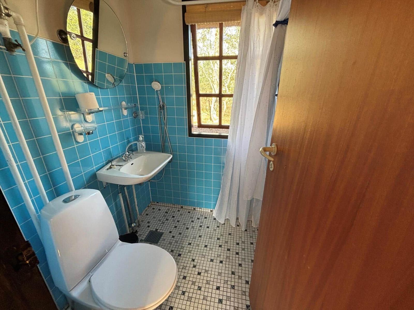 Bathroom with blue tiles, toilet, sink, and shower with window.