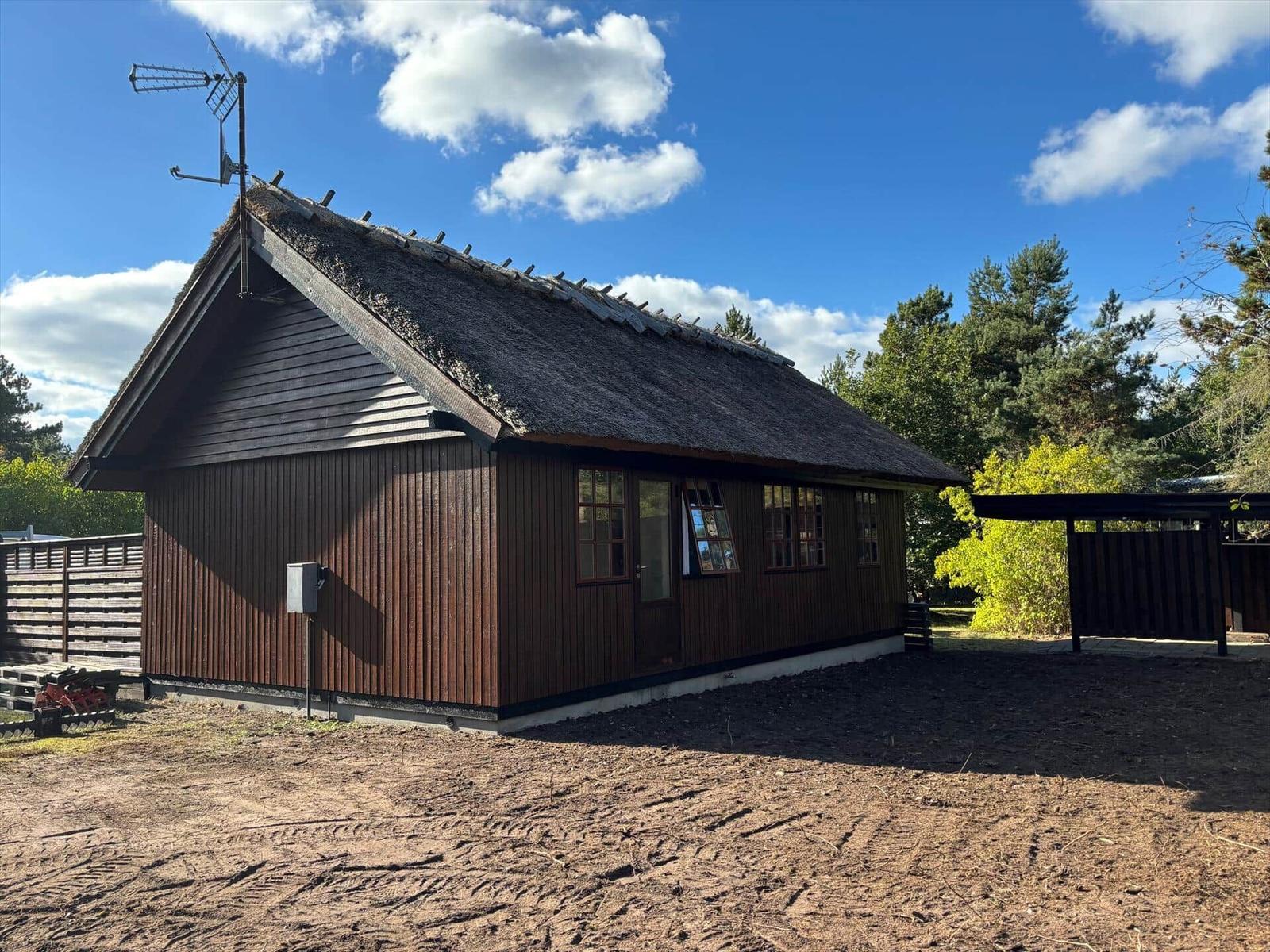 Wooden house with thatched roof and antenna under blue sky