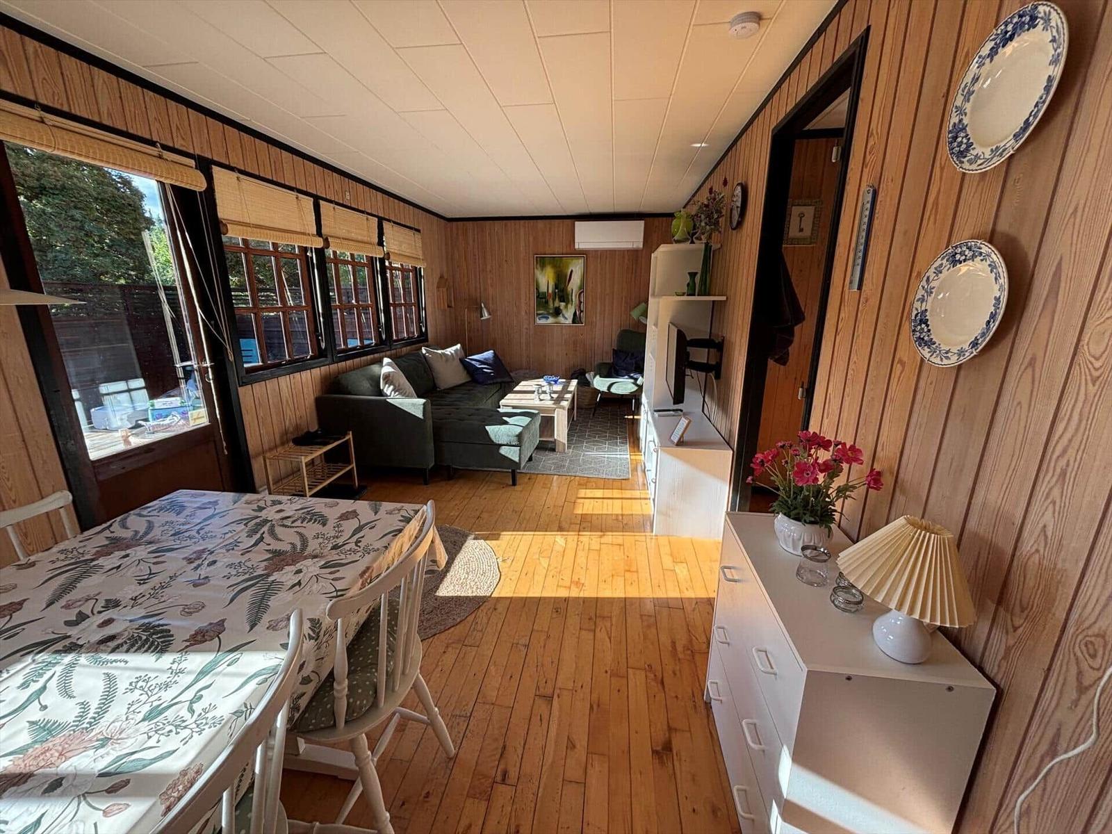 A room with dining area, sofa and wood paneling. Tables and chairs are present.